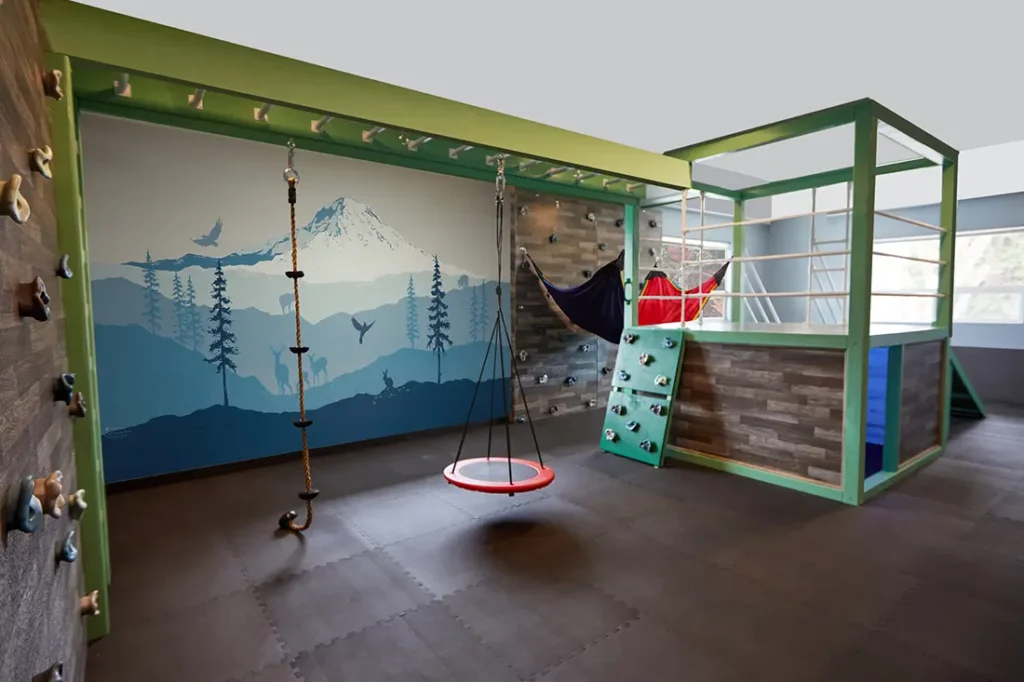 Sensory gym with nest swing, rope, climbing wall, and hammocks with a nature-themed mural